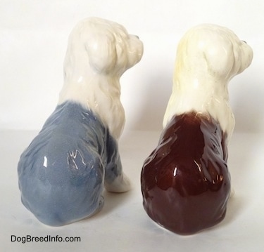 The back of two figurines of a porcelain Old English Sheepdogs that are in a seated position. The figurines are two different colors. One is blue and One is brown.