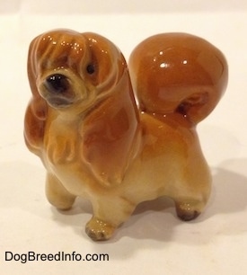 A brown with tan Pekingese figurine. The figurine has its hair covering one eye and the other eye is a black circle.
