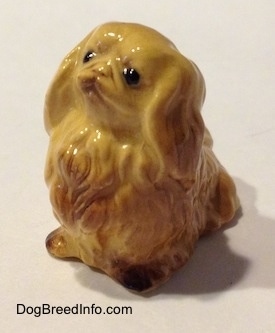 The front left side of a tan Pekingese figurine. The figurine has detailed black circles for eyes.