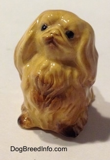 The front left side of a tan figurine of a Pekingese. The figurine is looking up.