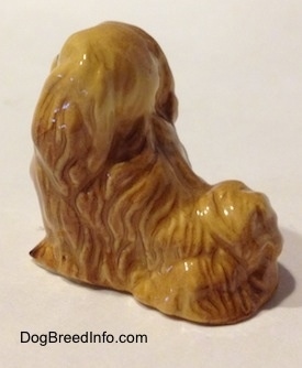 The back left side of a tan figurine of a Pekingese. The tail of the figurine is arched on its back.