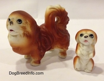 A brown with white Pekingese figurine and next to it is a brown with white Pekingese puppy figurine in a begging pose.