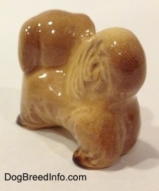 The back left side of a tan with brown Pekingese figurine. The ears of the figurine is hard to differentiate from the head.