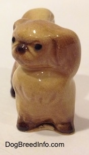 A figurine of a tan with brown Pekingese. The figurine turned its head to the left.