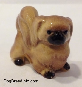 The front right side of a tan with brown Pekingese figurine. The figurine has black circles for eyes.