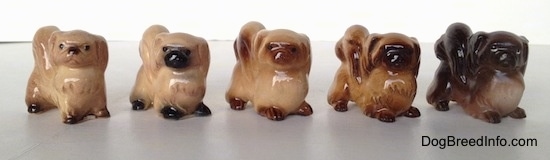 A line-up of different color variations of a Pekingese figurine. The figurines have black circles for eyes.