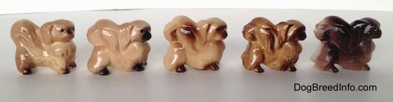 The right side of a line-up of different color variations of a Pekingese figurine. The tails of the figurines are arched across there backs.
