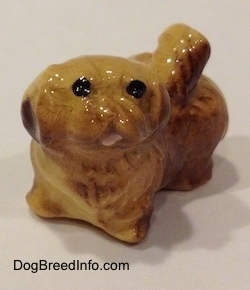 The front left side of a brown and tan figurine of a Pekingese puppy. The figurine has black circles for eyes.