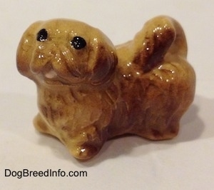 The left side of a brown and tan Pekingese puppy figurine. The figurine has its mouth painted open.