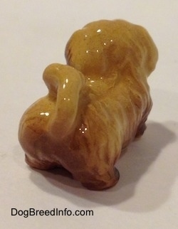 The back right side of a brown and tan Pekingese puppy figurine. The figurine has its tail arched onto its back.