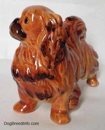 The front left side of a brown and tan with black Pekingese figurine. The figurine has black tipped ears.