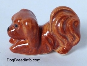The left side of a brown Pekingese figurine that is in a play bow pose. The figurine has fine hair details.