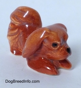 The front right side of a brown figurine of a Pekingese that is in a play bow pose. The figurine is glossy.