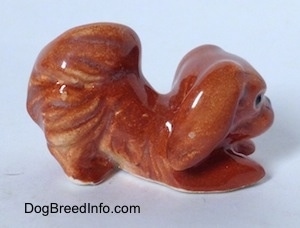 The right side of a brown Pekingese figurine that is in a play bow pose. The figurine has short legs.