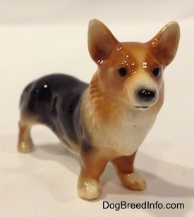 The front left side of a figurine that is a black and tan Pembrokw Welsh Corgi. This figurine has black circles for eyes.