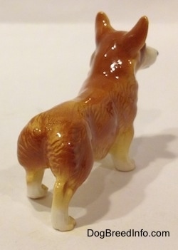 The back right side of a brown with white Pembroke Welsh Corgi. It is hard to tell the difference between the tail of the figurine fromt the body.