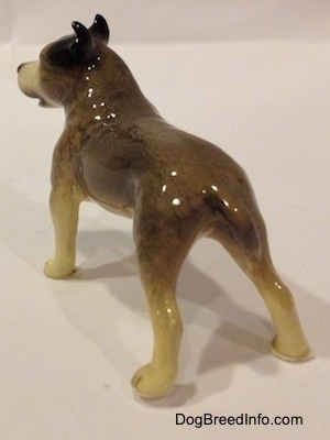 The back left side of a figurine of a black, gray and white Pit Bull Terrier figurine. The figurine has a small gray tail.