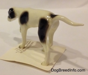 The back left side of a white with black Pointer in a pointing pose figurine. The figurine has a black spot at the base of its tail.