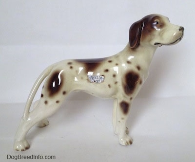 The right side of a white and tan Pointer with brown patches figurine. There is a silver sticker on the side and it has the word Pointer on it.