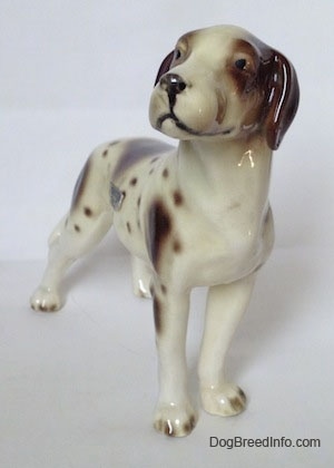 The front right side of a figurine of a white and tan Pointer with brown patches. The figurine has black circles for eyes.