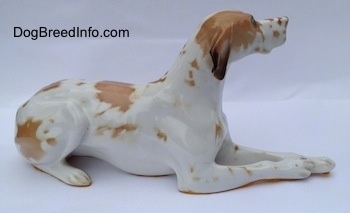 The right side of a porcelain white with brown Pointer in a lying pose figurine. The figurine has brown spots all over its body.
