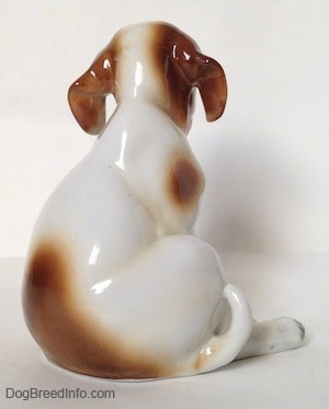 The back of a figurine of a Pointer puppy sitting with a fly on its nose. The figurine has a large brown spot at the bottom of its back.