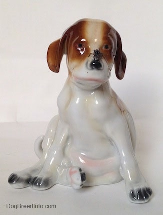 A figurine of a Pointer puppy sitting with a fly on its nose figurine. The figurine has black circles for eyes.
