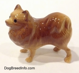 The left side of a brown with tan Pomeranian standing figurine. The figurine has a tail on its back.