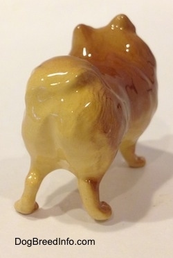 The back right side of a figurine of a brown with tan Pomeranian standing. The figurine has short tan legs.