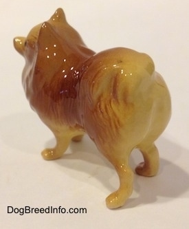 The back left side of a brown with tan figurine of a standing Pomeranian.