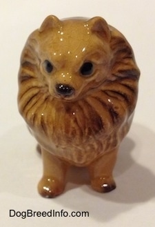 A figurine of a brown Pomeranian sitting. The figurine has hair around its head like a lions mane.