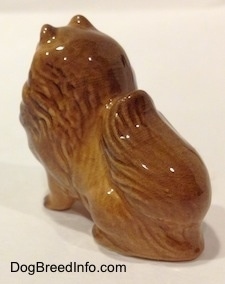The back left side of a figurine of a brown sitting Pomeranian. The Pomeranian has fine hair details.
