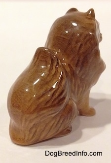 The back right side of a sitting brown Pomeranian figurine. The Pomeranian has short ears in the air.