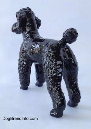 The back left side of a figurine of a black Poodle standing.