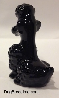 The back left side of a sitting black Poodle figurine. It is hard to differentiate the ears of the figurine from its head.