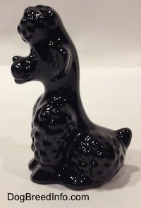 The left side of a figurine of a sitting black Poodle. The figurine has short legs.