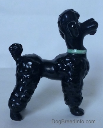 The right side of a black Poodle with a green collar figurine. Its hard to differentiate the ears of the figurine from its head.