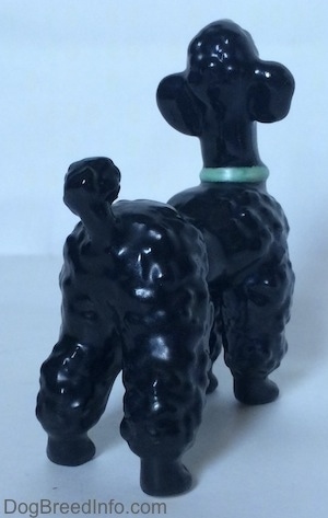 The back right side of a black figurine of a Poodle with a green collar. The figurine has a short tail with a large hair poof at the end.
