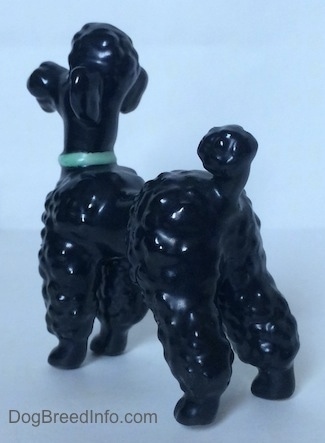 The back left side of a black Poodle figurine with a green collar.