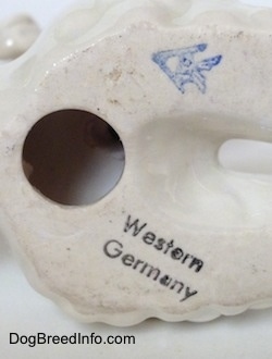 Close up - The underside of a Poodle figurine. There is a hole on the underside above the hole is a blue stamp of Goebel W. Germant and below the hole is a black stamp that reads 'Western Germany'.