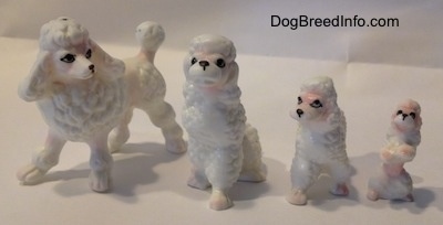 A white with pink bone china Poodle family. There are two adult figurines and two puppy figurines.