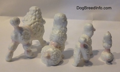 The back right side of four bone china Poodle figurines. Two of the figurines are in a sitting position.