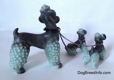 The right side of three porcelain figurines of Poodles chained together. All of the figurines tails are arched upwards in the air.