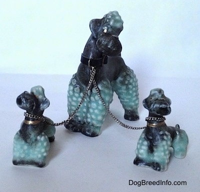 Three black with green Porcelain Poodles chained together figurines. The biggest figurine has a black leather collar on.