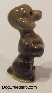 The right side of a figurine of a miniature gray Poodle in a begging pose. The figurine has black circles for eyes and a nose.