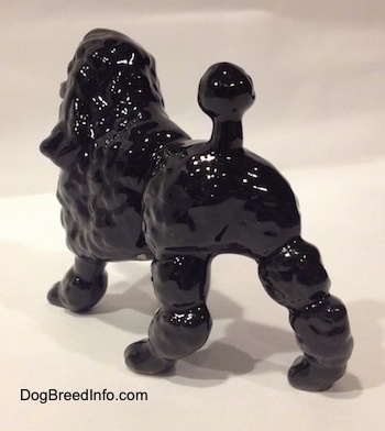 The back right side of a black porcelain Poodle figurine. The figurine has a tail with a hair poof at the end of it.