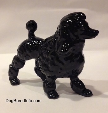 The front right side of a porcelain figurine of a black Poodle. The figurines upper half is a hair poof.