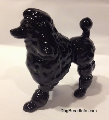 The front left side of a black porcelain figurine of a Poodle. The figurine has long legs.
