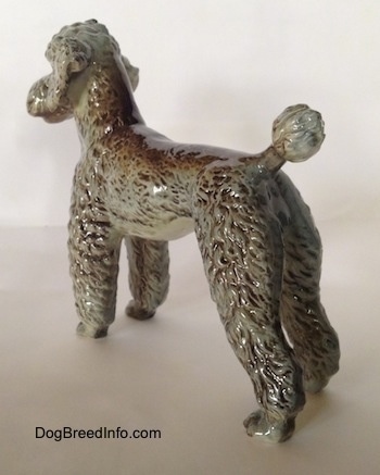 The back left side of a black, gray and brown figurine of a Poodle standing.
