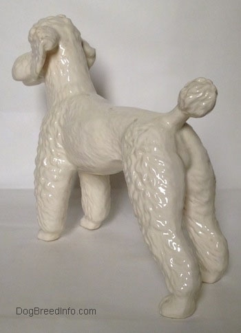 The back left side of a figurine of a white Poodle. The figurine is glossy.